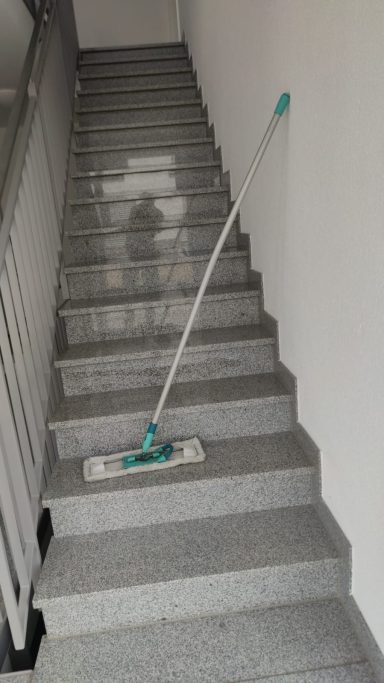 Treppenhausreinigung Wangen im Allgäu Bodenwischer steht auf einer grauen Treppe mit weißen Wänden.