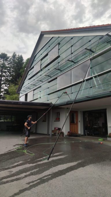 Fassade Reinigung Ein Mann reinigt eine Glasfassade eines modernen Gebäudes mit einem Hochdruckreiniger.
